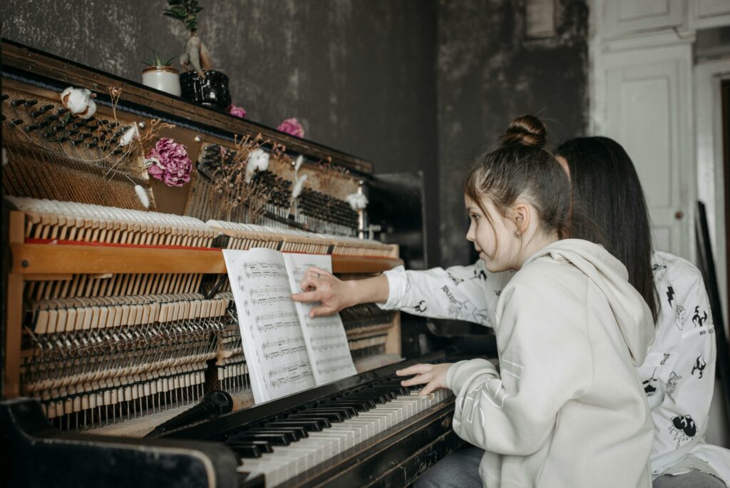 A young girl receiving piano lessons from a teacher. Indoor music education setting.